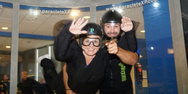 Woman and instructor smile and point at the camera in the Paraclete XP wind tunnel.