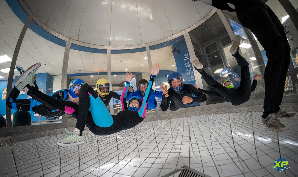 A group of indoor skydivers in various positions smiling at the camera.