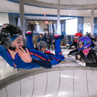 Three women fly in the tunnel on their bellies with their hands in front of them.