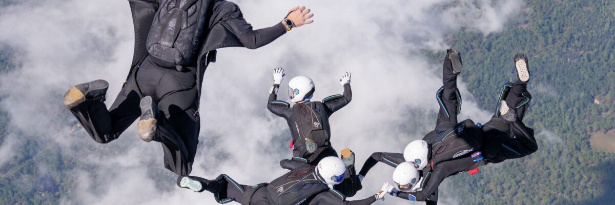 A 4 way skydiving team and their videographer all wearing black jumpsuits in freefall.