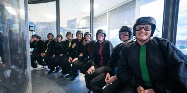 Group of indoor skydivers in jumpsuits and goggles prepare to enter the tunnel
